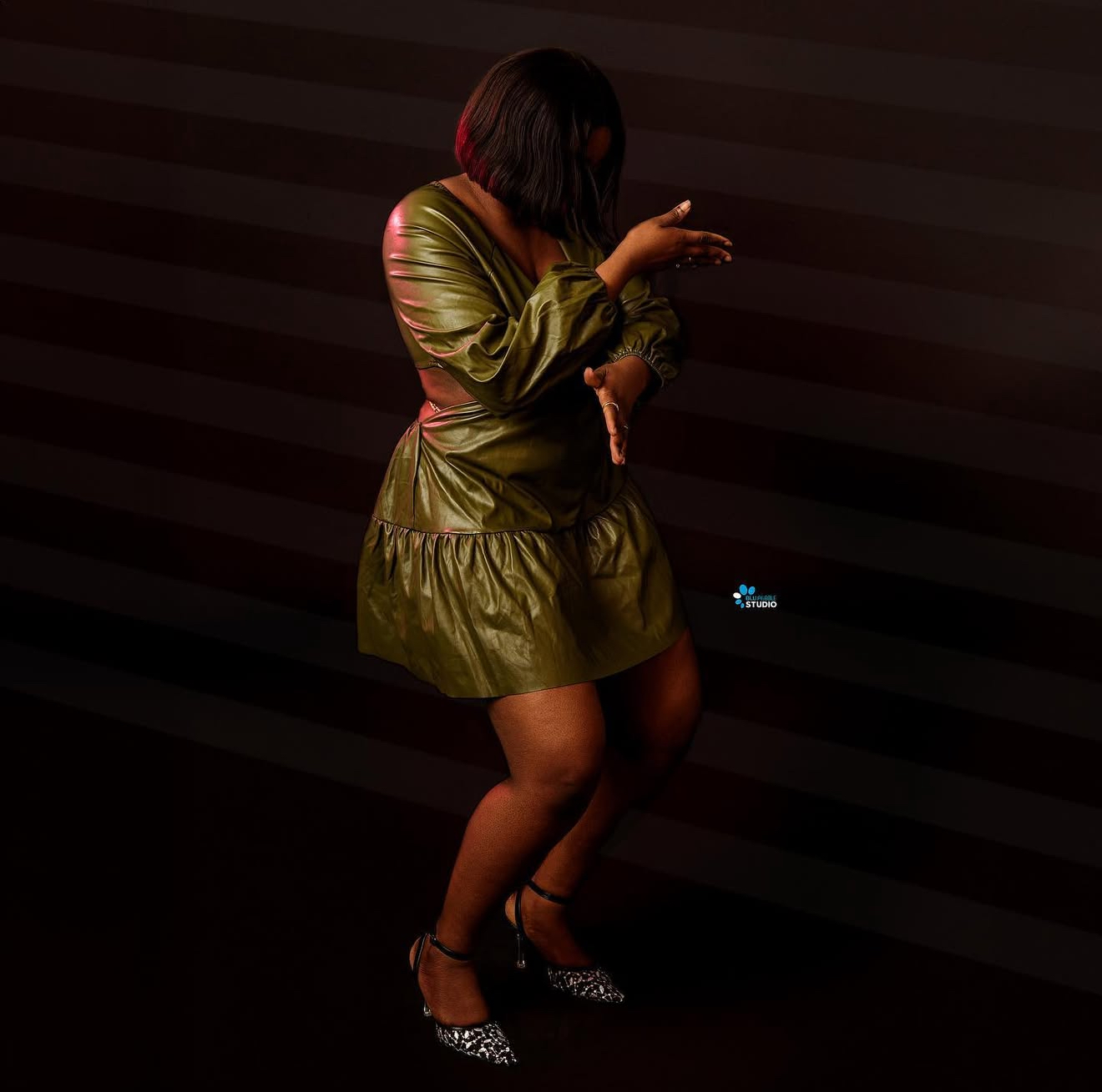 Woman in an olive satin dress dancing in dramatic low light against a striped wall