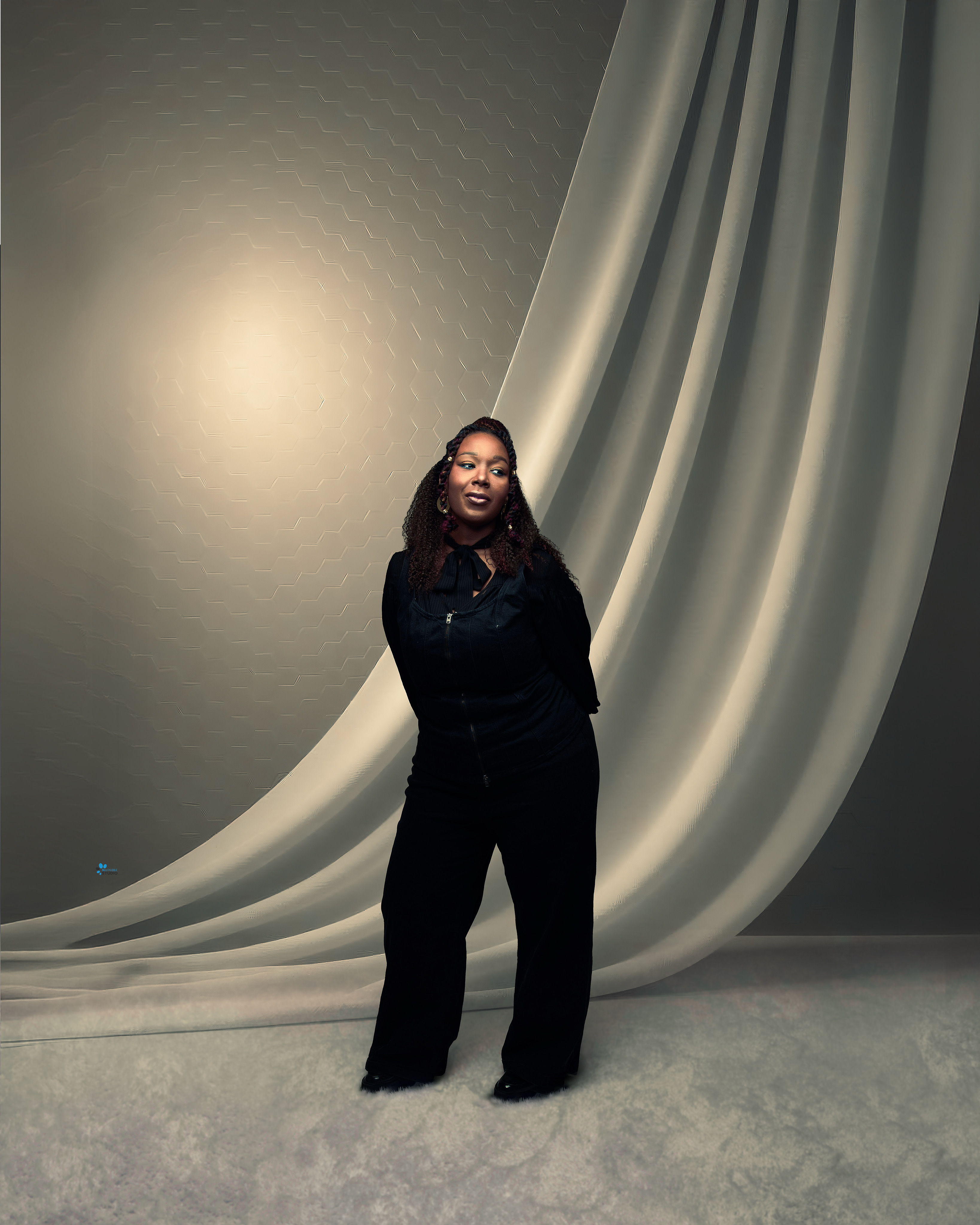 Woman in a black zip-front outfit standing in soft light against draped grey fabric