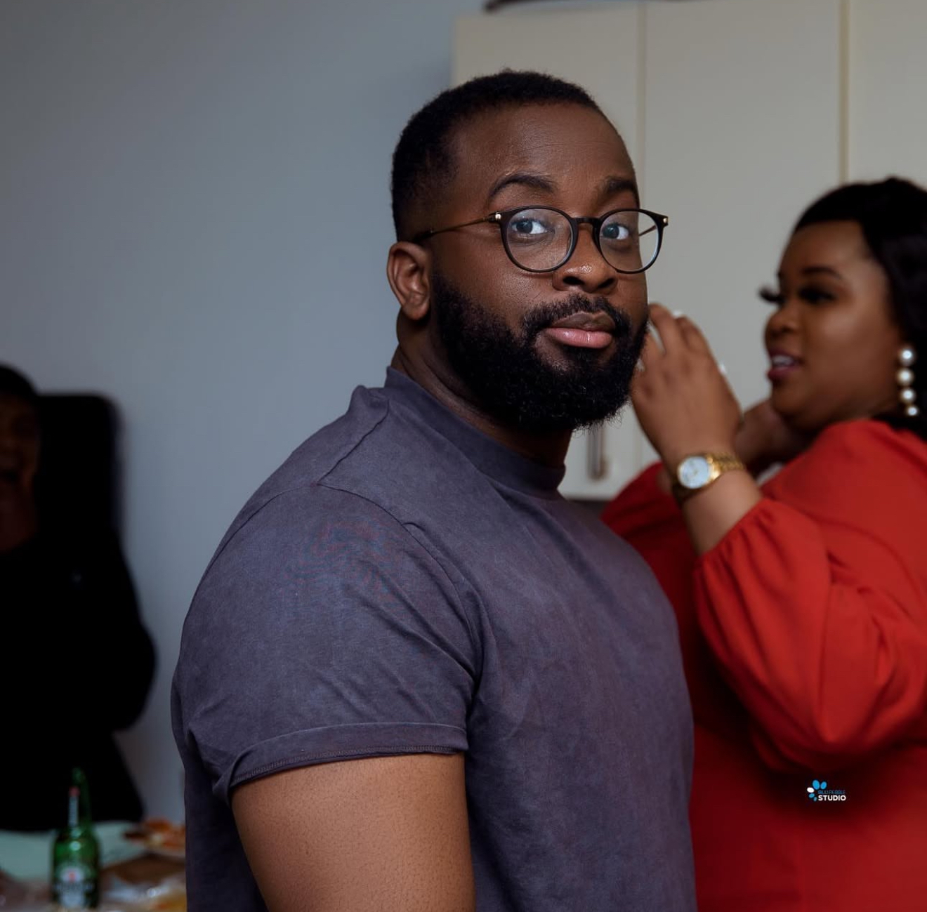 Man in glasses and a grey tee glancing over his shoulder at an indoor gathering