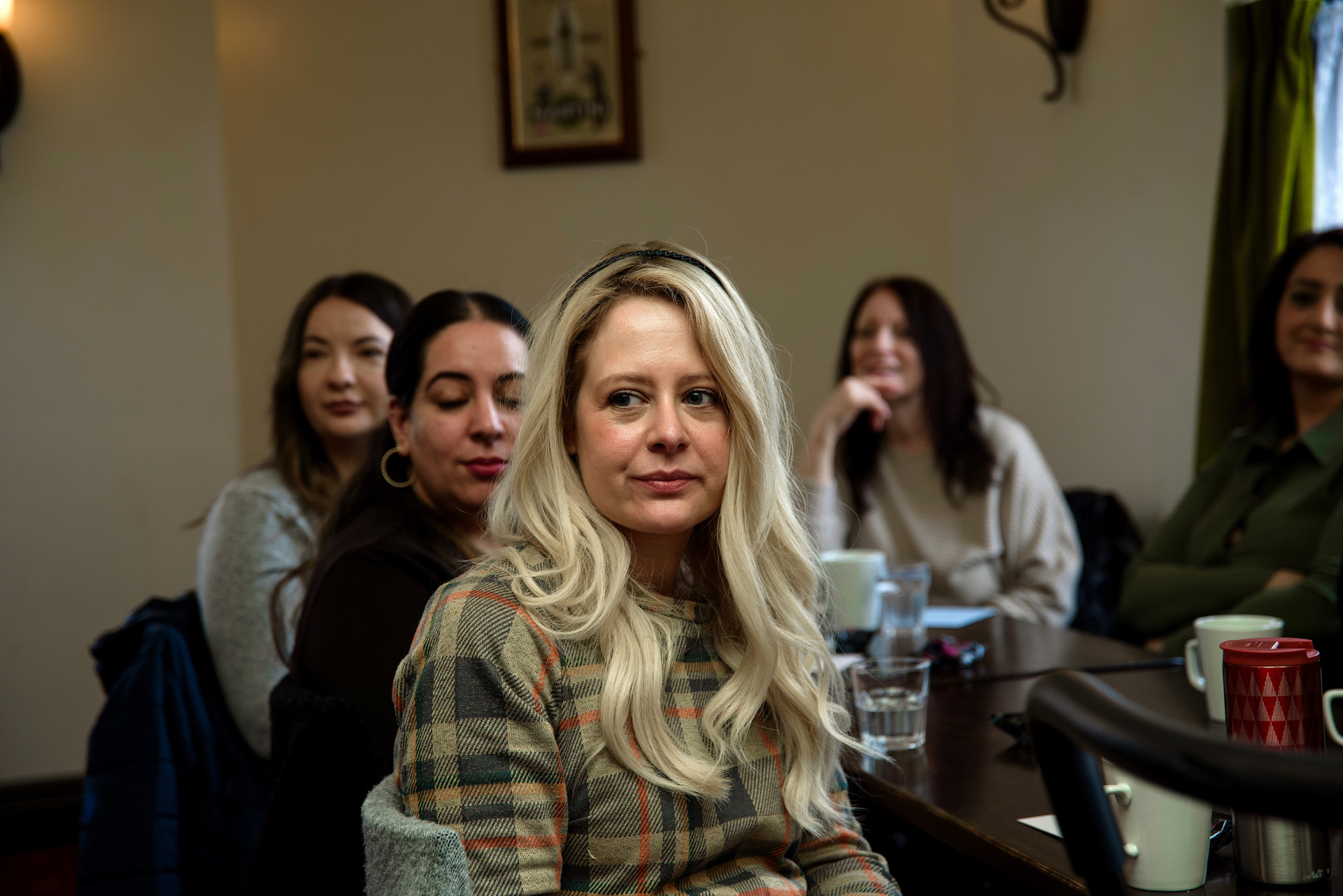 Blonde guest in a plaid jumper seated among a group of attendees around a long table