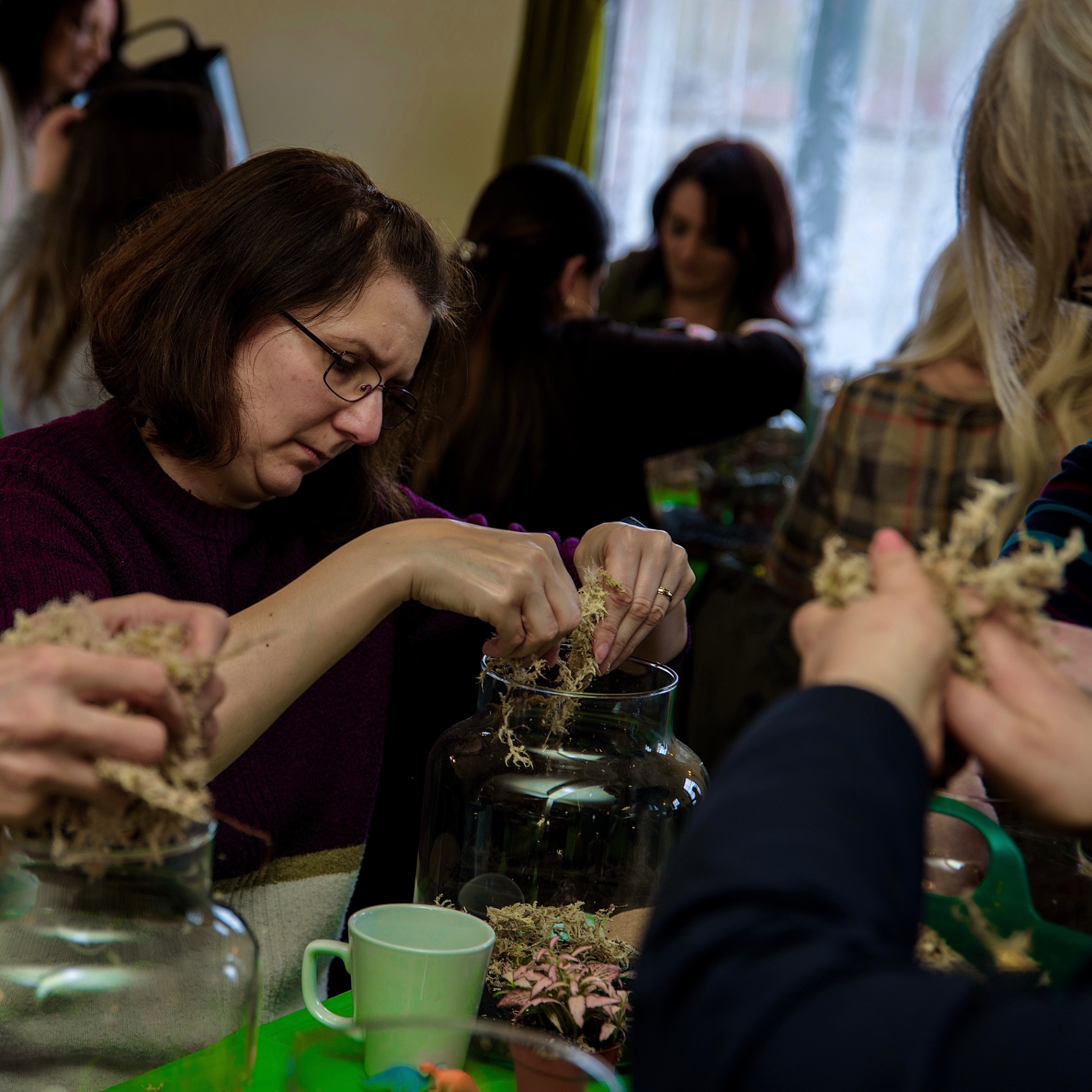 Woman in glasses packing moss into a glass jar during a terrarium building workshop