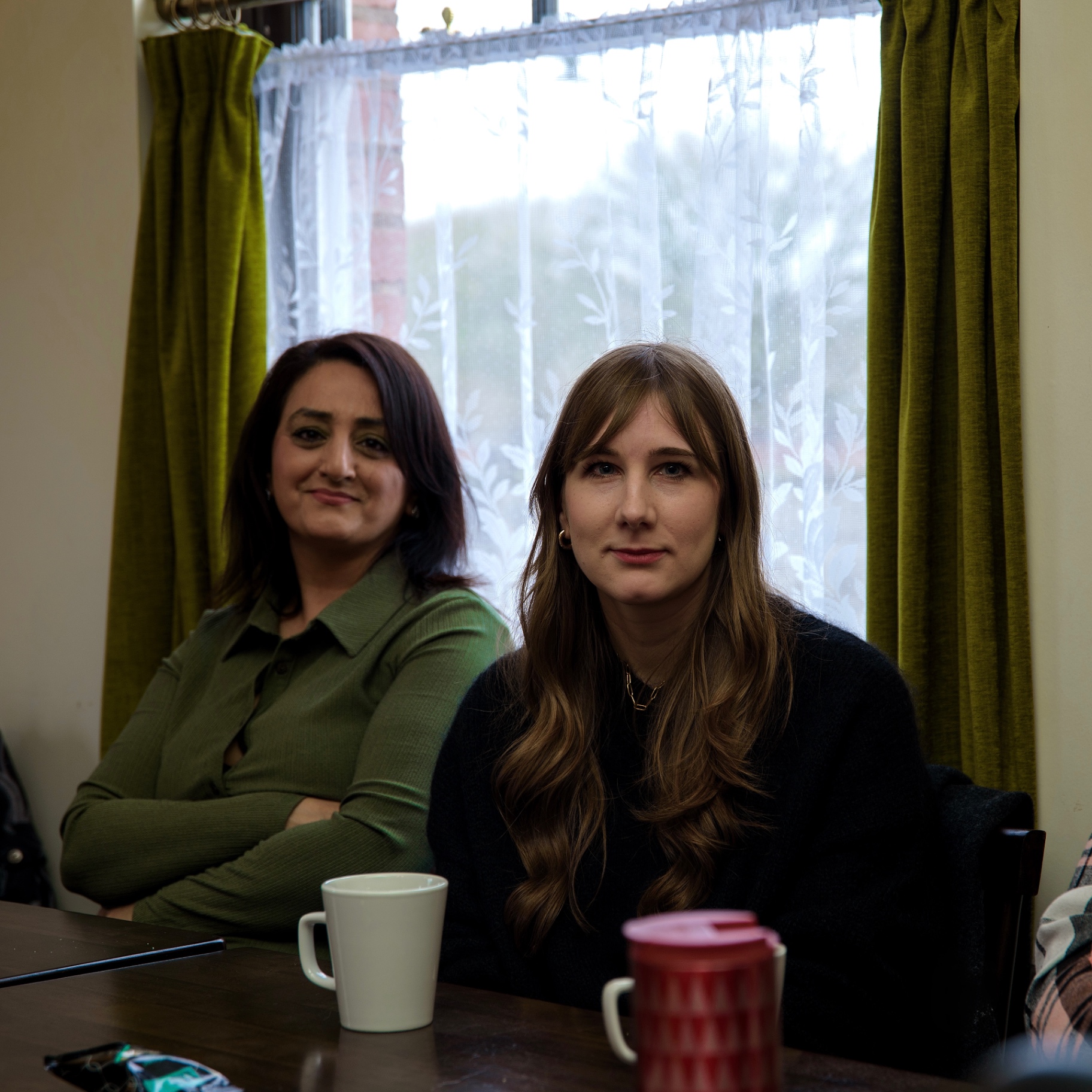 Two guests seated at a table by a curtained window looking towards the camera