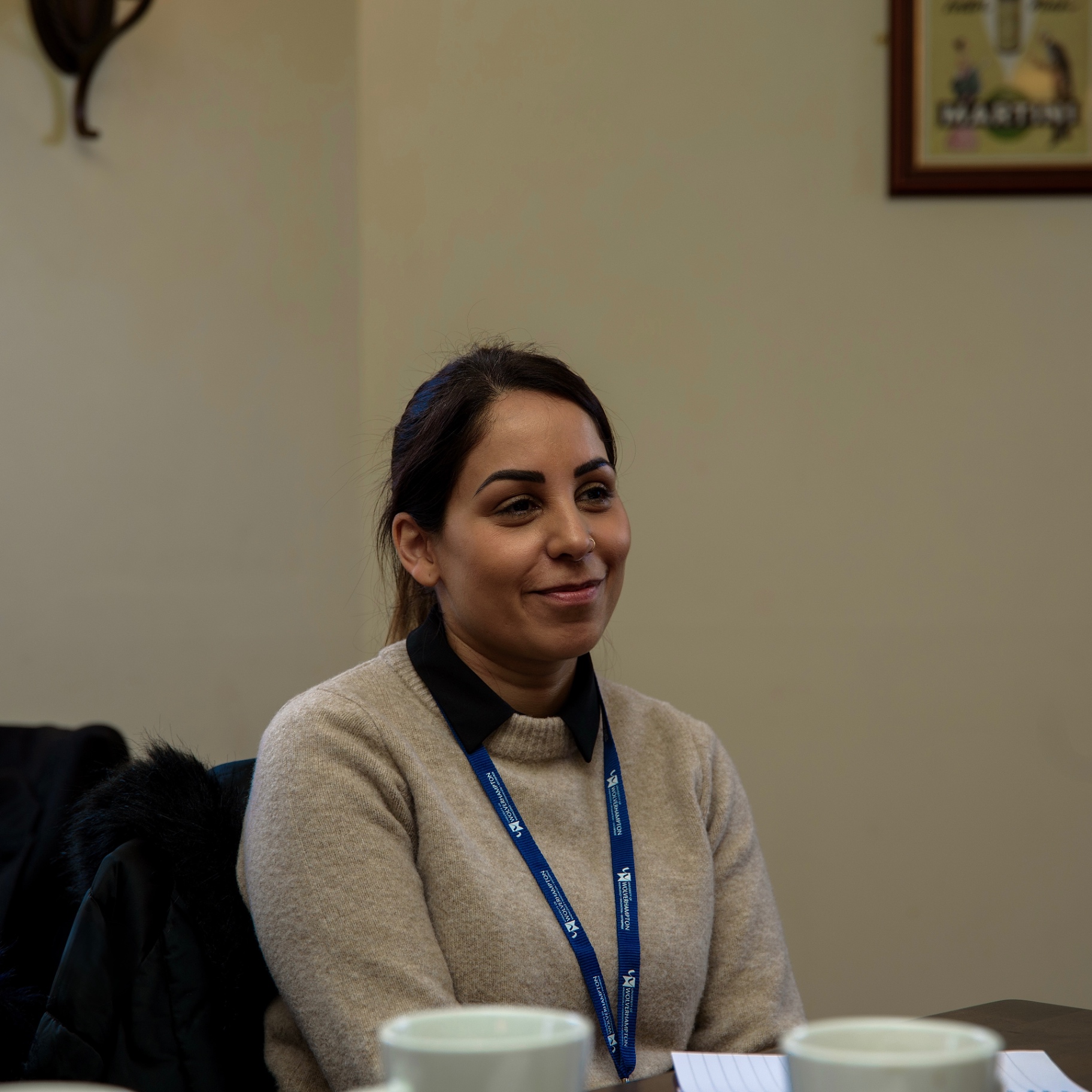 Woman in a cream jumper and lanyard smiling while listening during an event