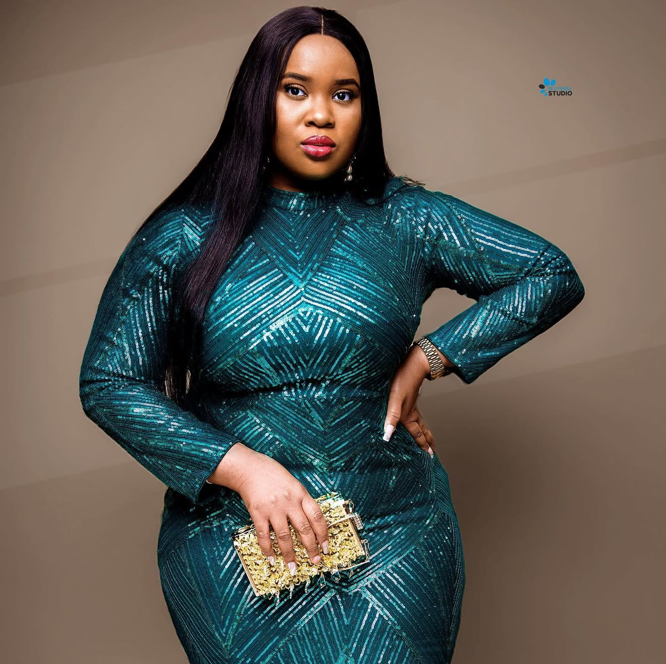 Woman in a teal sequin gown holding a gold clutch against a warm taupe studio backdrop