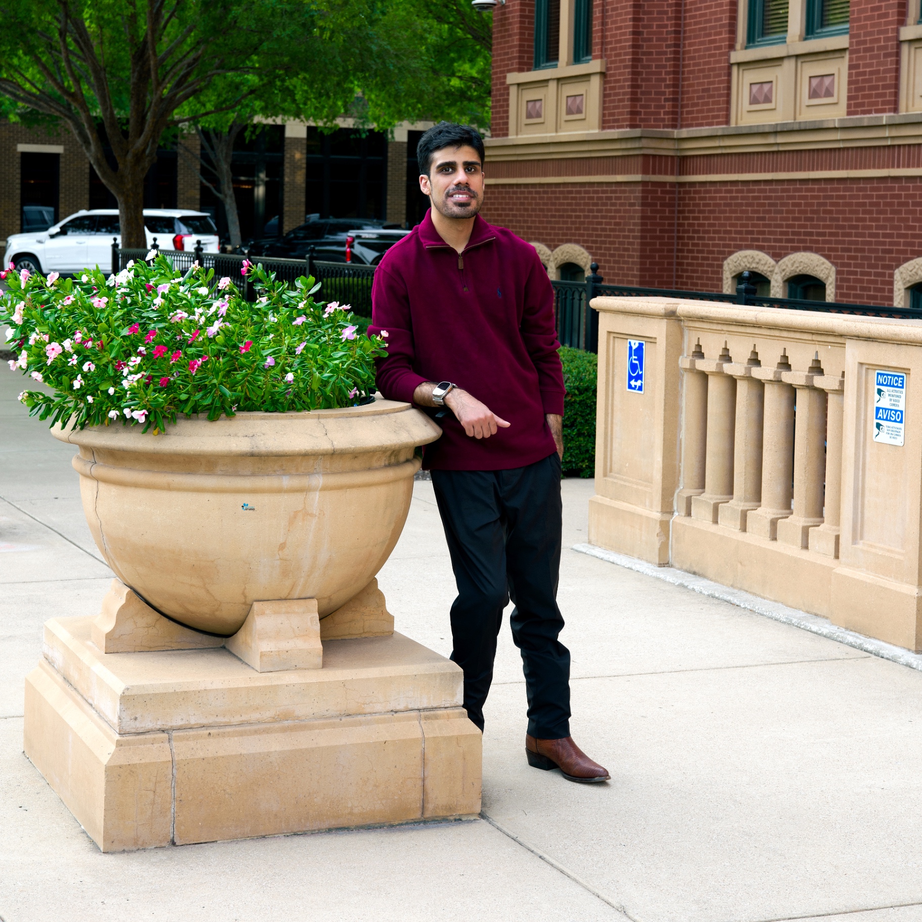Man in a burgundy quarter-zip leaning on a large stone planter on a city sidewalk
