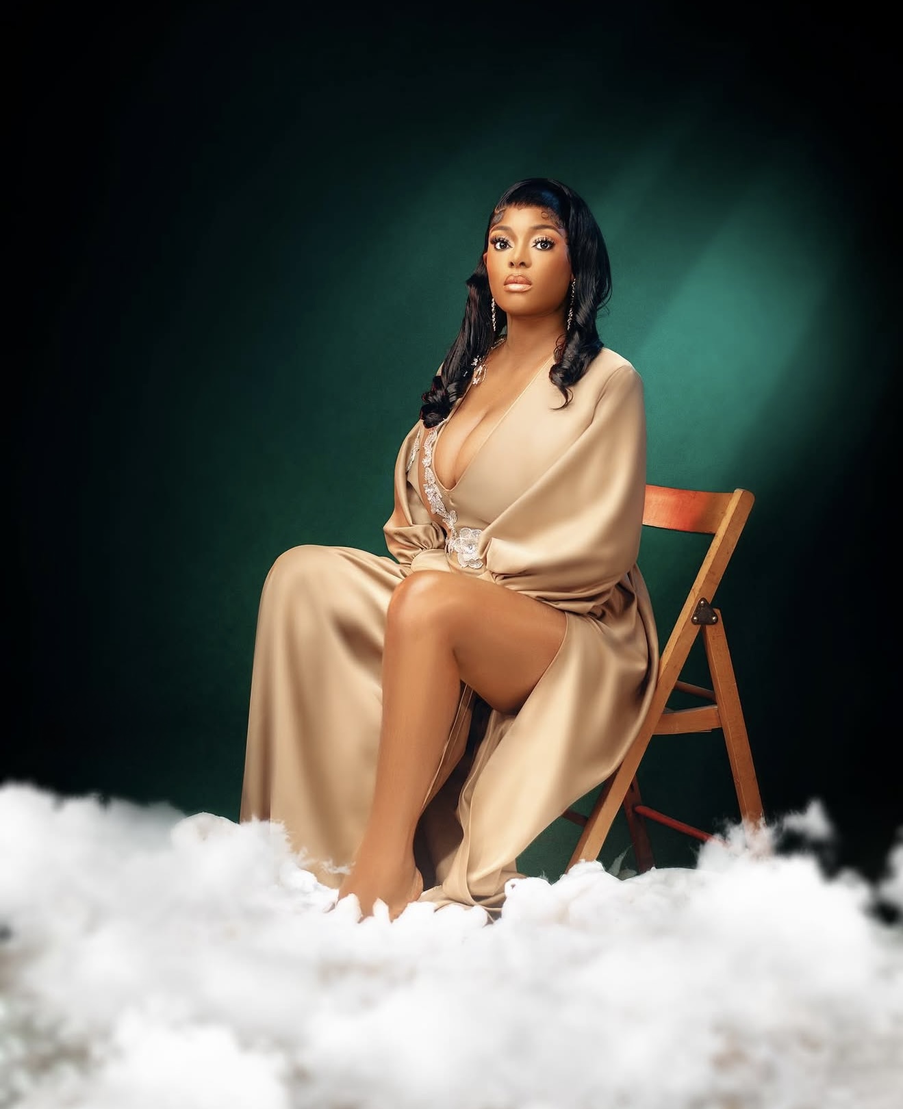 Woman in a champagne satin gown seated on a wooden chair above white clouds